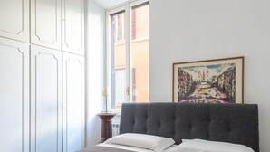 A neatly made bed with a grey headboard, white pillows, and a grey quilted bedspread. There is a framed abstract painting on the wall above the bed. - Virgilio by Interhome (Roma: Piazza Navona - Campo dei Fiori)