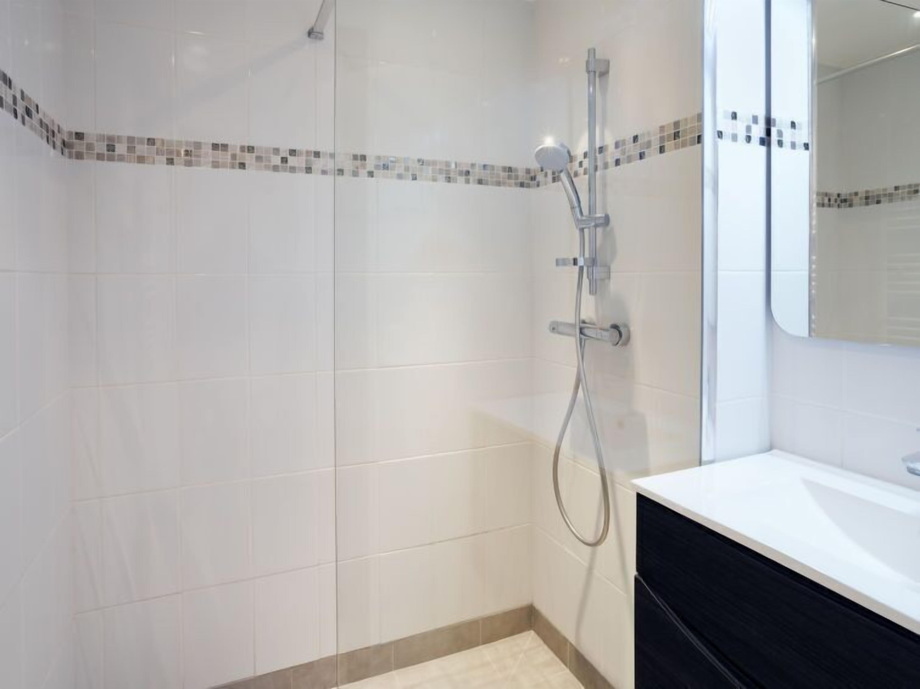 Een moderne badkamer met douche, betegelde wanden en een spiegel.