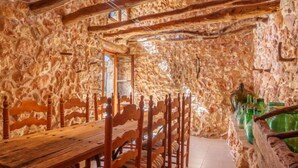 A rustic interior with a stone wall, wooden ceiling beams, a wooden dining table, and chairs. - Can Xerret by Interhome (Sencelles)