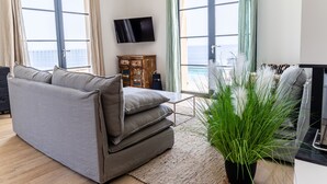 A living room with a grey sofa, a wooden cabinet, a flat-screen TV, and a view of the sea through large windows. - Villa NEPITA, swimming pool, sea view for 8 people, 4 bedrooms, ERBALUNGA, 20222 (Brando)
