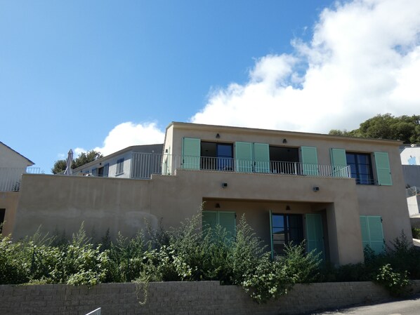 A two-story building with a flat roof, a balcony with a metal railing, and a brick wall in the foreground. - Villa NEPITA, Pool, Ocean View, Sleeps 8, 4 Bedrooms, ERBALUNGA, 20222 (Brando)
