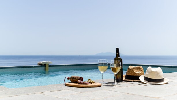 A poolside setting with a view of the sea, a bottle of wine, two glasses, a hat, and a wooden board with food items. - Villa NEPITA, swimming pool, sea view for 8 people, 4 bedrooms, ERBALUNGA, 20222 (Brando)