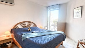 Een slaapkamer met een bed, nachtkastje, lamp, airconditioning en uitzicht door een raam.