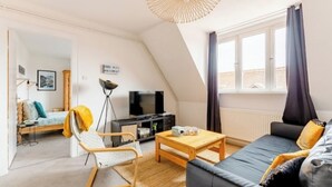 Una sala de estar moderna estilo loft con techo inclinado, un sofá, una mesa de centro de madera, un televisor y una silla.