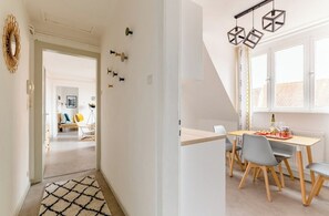 A modern dining area with a wooden table, grey chairs, and a hanging light fixture. - 2-room apartment. Right in the historic city center! (Sélestat)