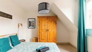 Un dormitorio con una cama, un armario de madera, una lámpara colgante y un cuadro en la pared.