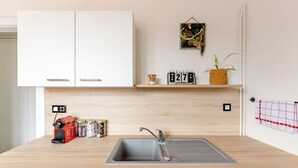 Una cocina con un lavabo, armarios, un calendario, una planta y una cafetera.
