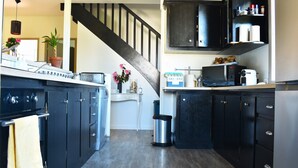 Cucina con pensili scuri, piano cottura in acciaio inossidabile, forno a microonde e cestino.