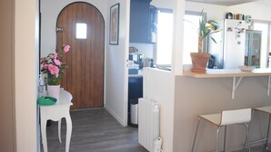 Una cucina con un frigorifero bianco, una porta di legno, una pianta in vaso e una sedia bianca.
