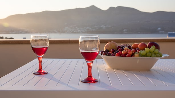 Deux verres de vin rouge sur une table blanche, avec un saladier rempli de fruits.