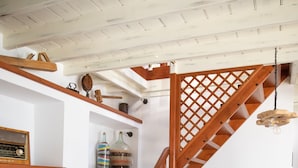 Un escalier en bois orné d’un motif en treillis, une table à manger avec des chaises, et un coin cuisine avec des étagères et des placards.