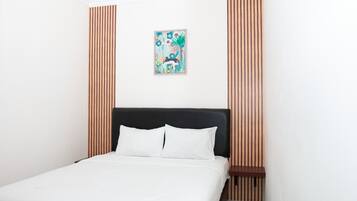 Ein ordentlich gemachtes Bett mit weißen Leinen in einem Raum mit vertikalen Holzpaneelen an den Wänden.