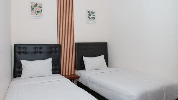 A room with two beds, each with a black headboard and white bedding. There is a wooden panel divider between the beds.
