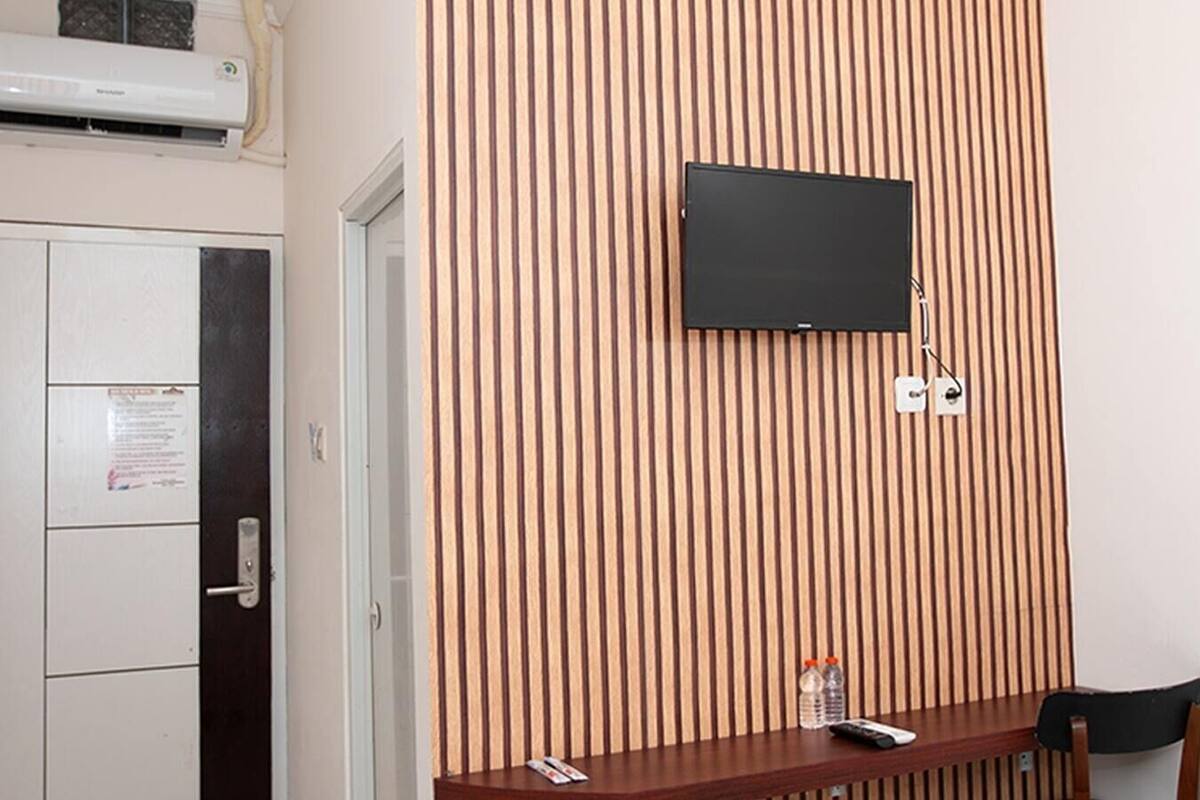 Une pièce avec un mur recouvert de lambris en bois, un téléviseur à écran plat fixé au mur, un bureau en bois avec une chaise et une porte avec une pancarte.