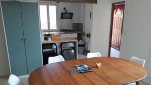 A dining area with a wooden table, white chairs, and a kitchen in the background.