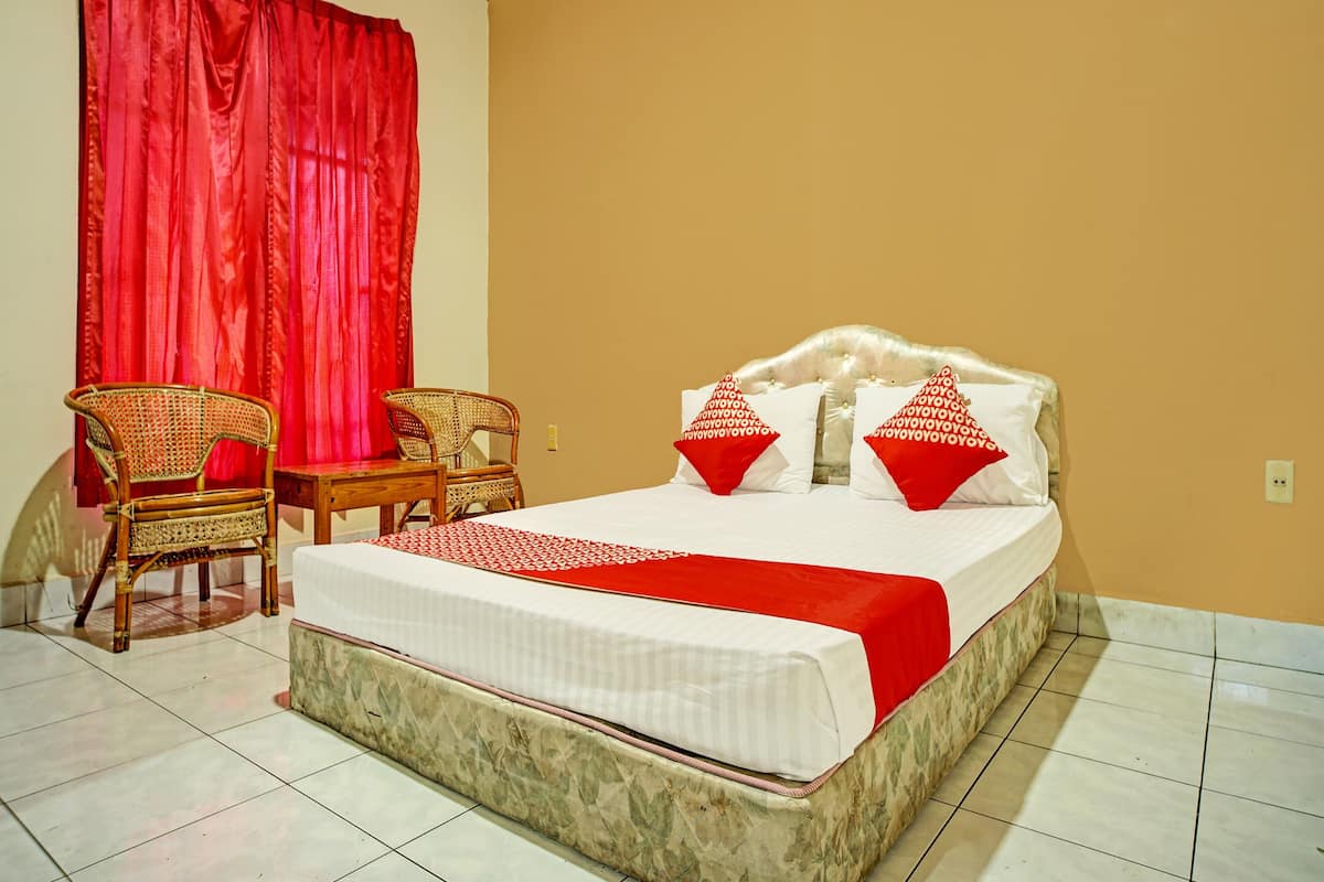 Ein Hotelzimmer mit einem Bett, zwei Stühlen, einem roten Vorhang und einer beige gefärbten Wand.