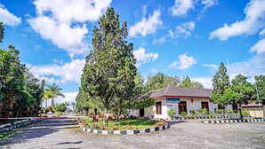 A building with a red roof and white walls, surrounded by a gravel area and trees. - Capital O 92214 Beristera Hotel (Kota Sidikalang)