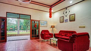 A lobby with red upholstered chairs, a tiled floor, a wall clock, and a door leading outside. - Capital O 92214 Beristera Hotel (Kota Sidikalang)
