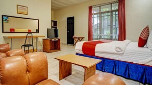 A hotel room with a bed, a desk, a television, leather chairs, and a window with curtains. - Capital O 92214 Beristera Hotel (Kota Sidikalang)