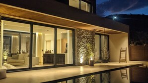 Ein modernes Haus mit Glasfassade, einer Steinsäule und einer kleinen Außen-Sitzgelegenheit.