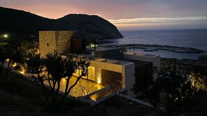 Ein modernes Gebäude an der Küste mit Steinwänden und großen Fenstern, mit Blick auf das Meer und einen felsigen Hügel.