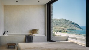 Ein modernes Badezimmer mit großem Fenster, einer Badewanne und Blick auf eine gebirgige Küstenlandschaft.