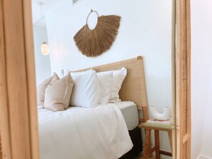 Un dormitorio con cama, almohadas, una mesita de noche con un libro y un adorno en la pared.
