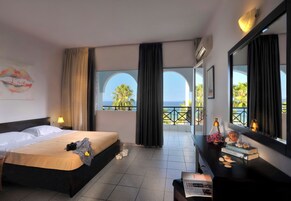 A hotel room with a bed, a desk, a mirror, and a view of the sea.