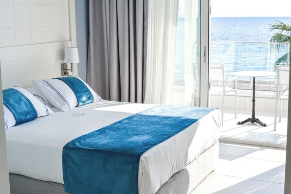 Ein Hotelzimmer mit einem großen Bett, einem Balkon mit Tisch und Stühlen und Meerblick.