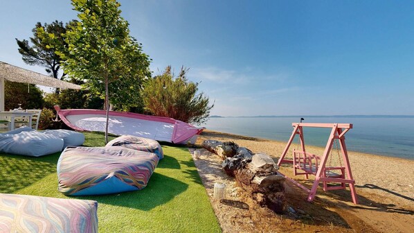 A beachside setting with a swing, colorful cushions, and a boat. - Acrotel Lilyann Boutique Hotel (Sithonia)