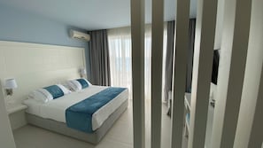 A hotel room with a large bed, a flat-screen TV, a window with curtains, and an air conditioning unit on the wall. - Acrotel Lilyann Boutique Hotel (Sithonia)