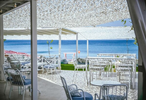 Zona de estar al aire libre con mesas y sillas, una sección cubierta y vista al mar.