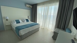 A hotel room with a bed, a desk, a chair, and a window with curtains. - Acrotel Lilyann Boutique Hotel (Sithonia)