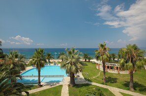 Zona de piscina con palmeras, cielo despejado y vista al océano.