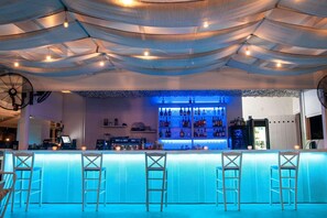 A bar area with a counter, bar stools, and a well-stocked shelf of bottles. - Acrotel Lilyann Boutique Hotel (Sithonia)