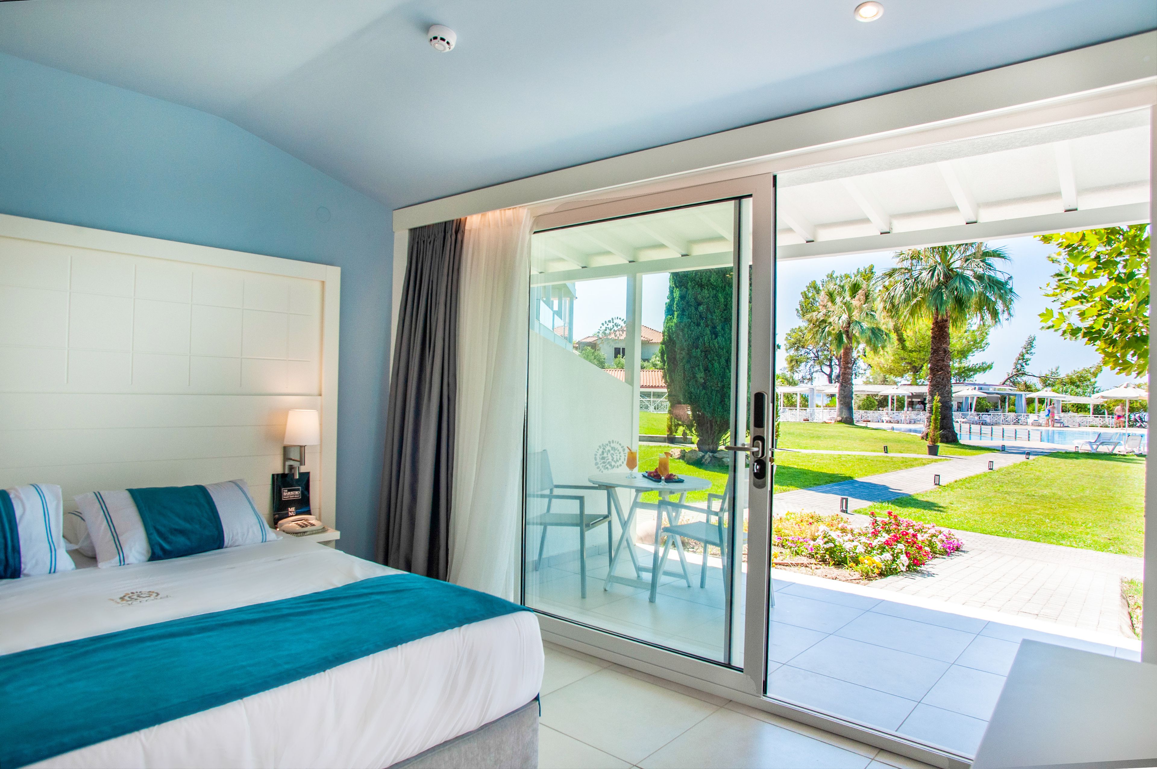 Ein Schlafzimmer mit einem großen Bett, einer Schiebetür zu einer Terrasse mit Pool und Gartenmöbeln.