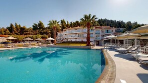 A swimming pool with lounge chairs and umbrellas, surrounded by multi-story buildings with balconies. - Acrotel Lilyann Boutique Hotel (Sithonia)