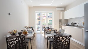 Een moderne keuken met witte kasten, een eethoek met twee stoelen en een uitzicht op balkons door glazen deuren.