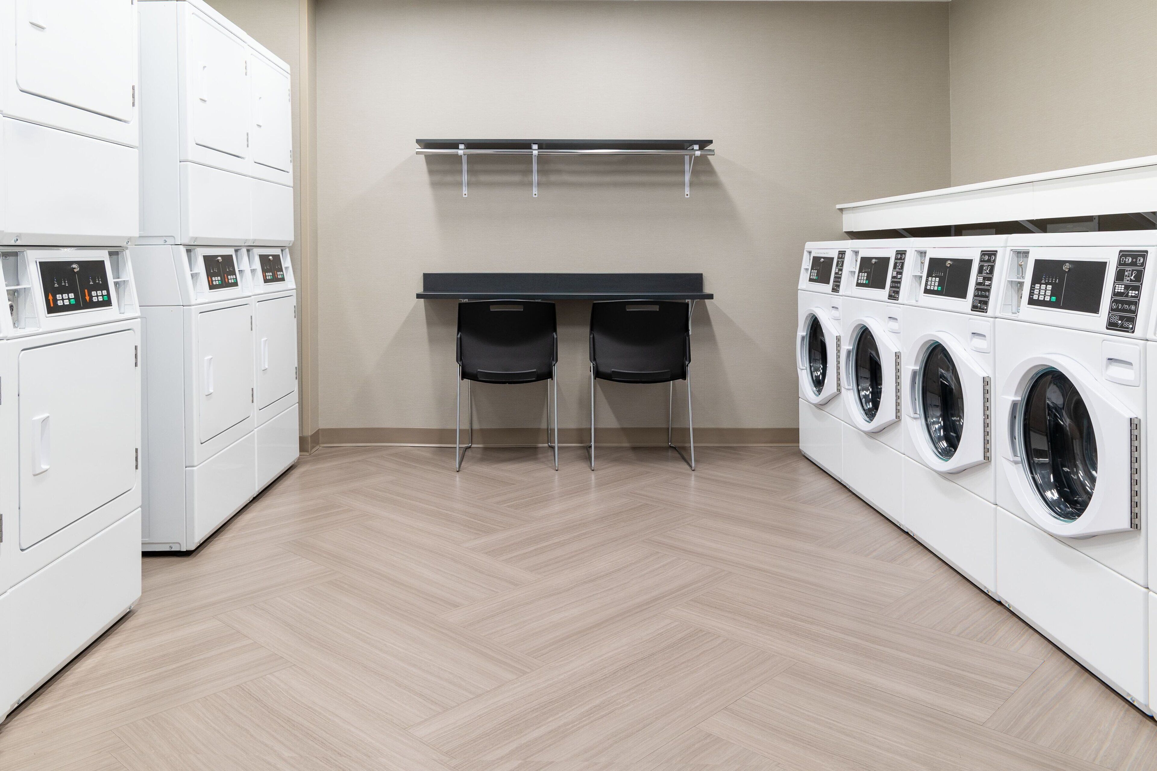 A laundry room with white washing machines, a table with chairs, and a wall-mounted drying rack.