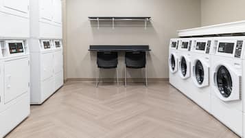 A laundry room with white washing machines, a table with chairs, and a wall-mounted drying rack.
