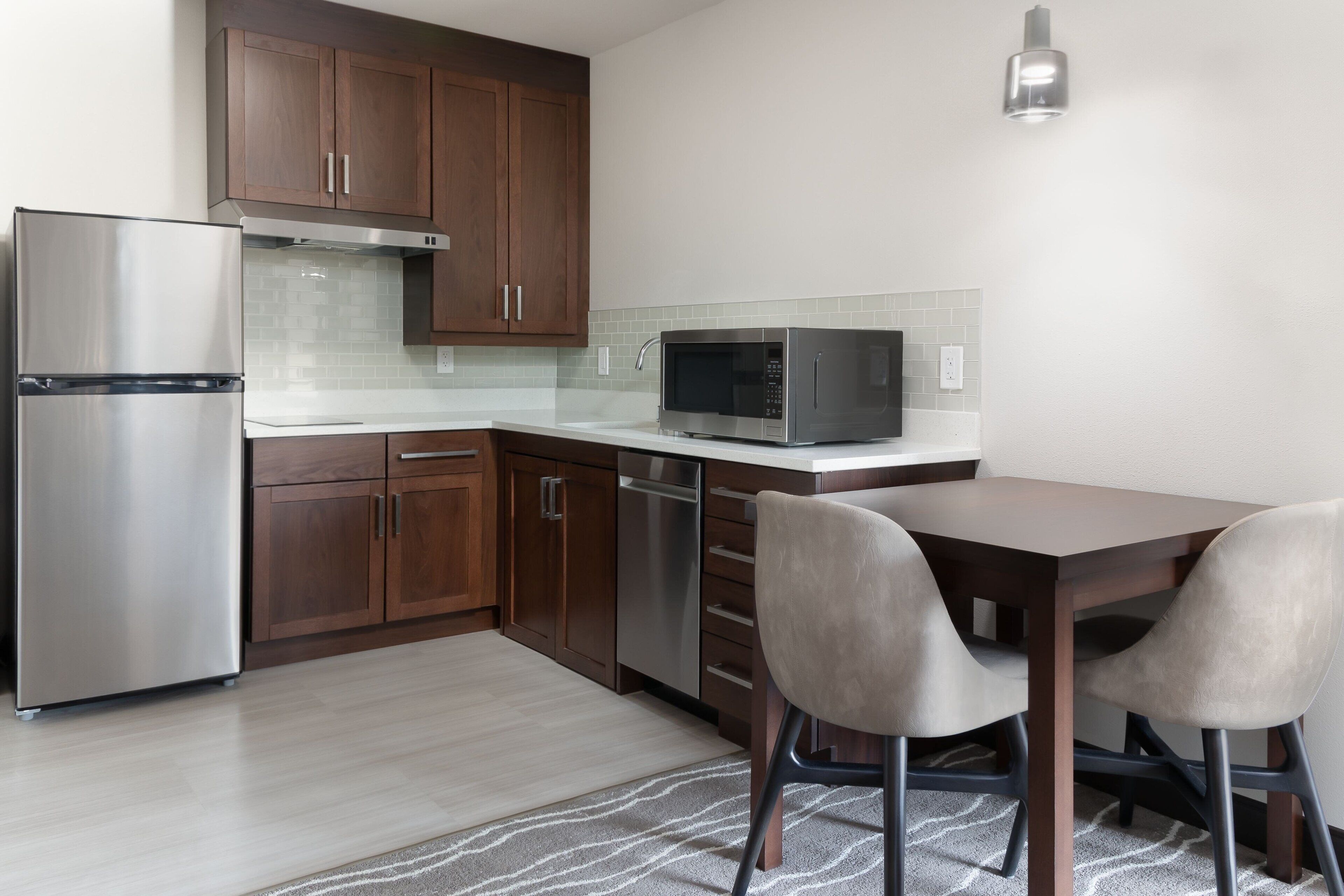 Una cocina moderna con armarios de madera, electrodomésticos de acero inoxidable y una zona de comedor con dos sillas.
