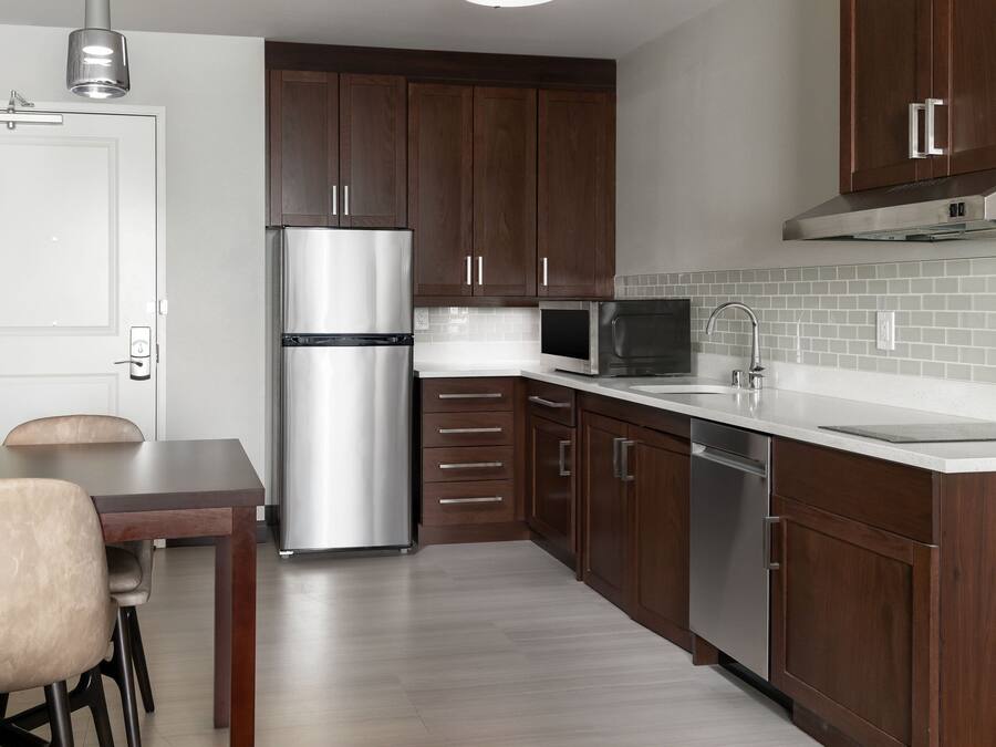 A modern kitchen with dark wooden cabinets, stainless steel appliances, and a white countertop.