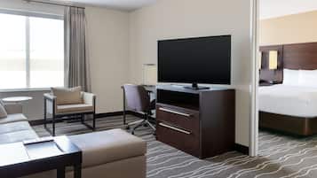 A hotel room with a bed, a TV, a desk, a chair, a sofa, and a small table.