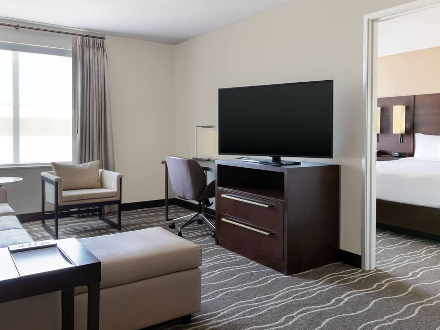 A hotel room with a bed, a TV, a desk, a chair, a sofa, and a small table.