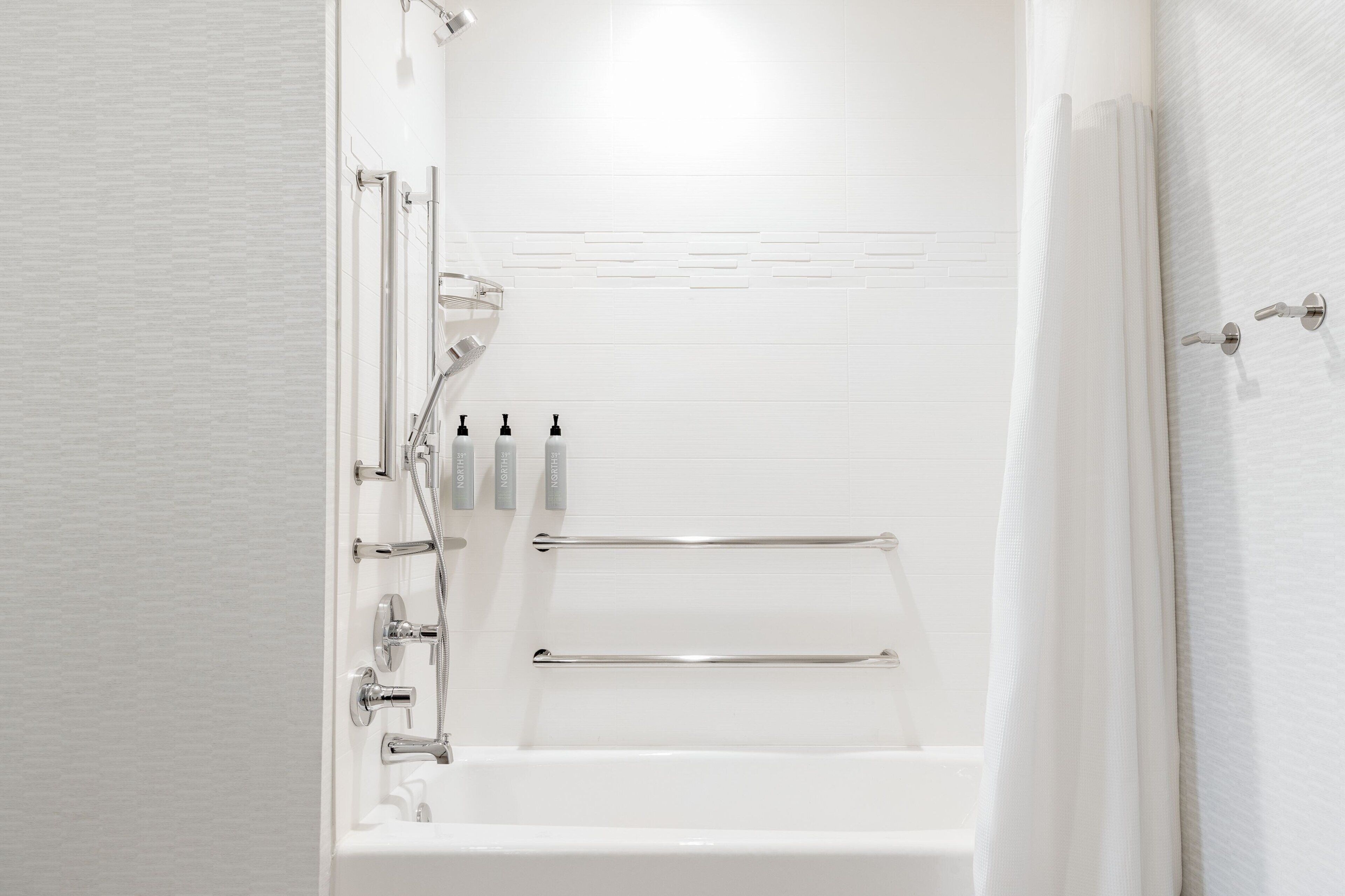 A modern bathroom with a bathtub, shower, and handrails.