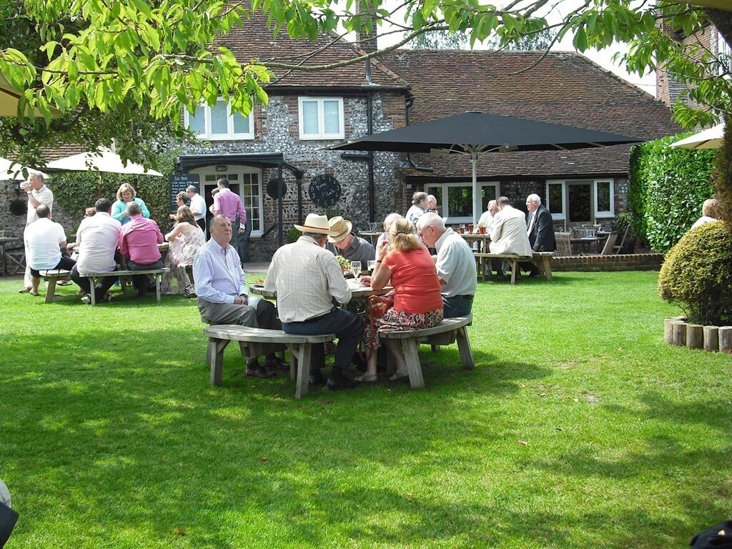 A group of people seated at outdoor tables in a garden area with a building in the background.