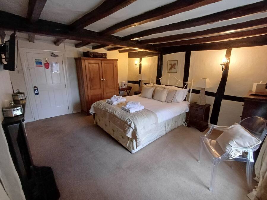 A bedroom with a large bed, wooden wardrobe, bedside table, and a clear plastic chair.