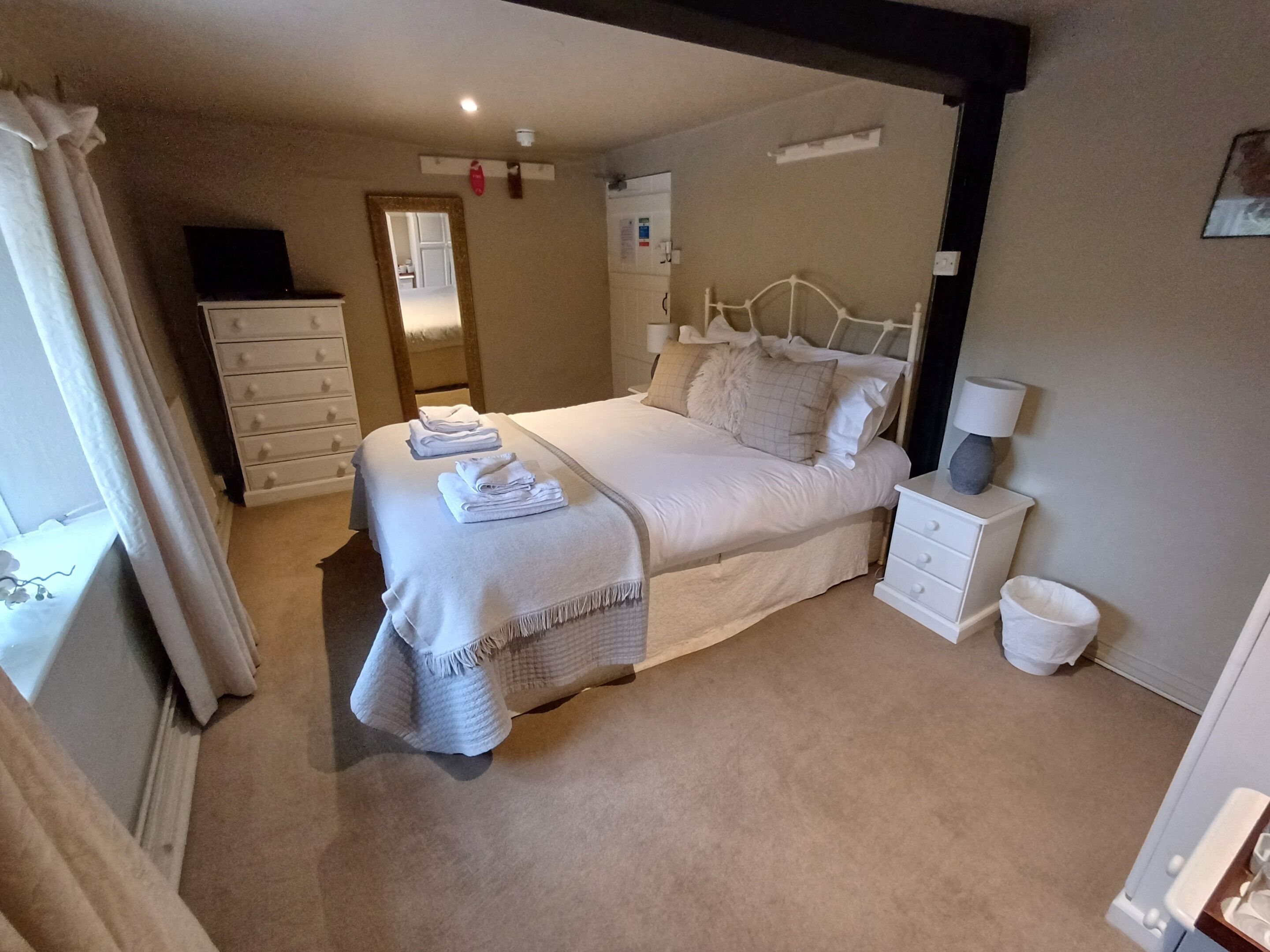 Une chambre bien rangée, avec un lit, des tables de chevet, une commode et une fenêtre avec des rideaux.