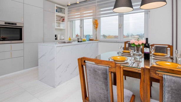 Una cocina moderna con una isla de mármol, un comedor con sillas de madera y un ventanal con vistas.