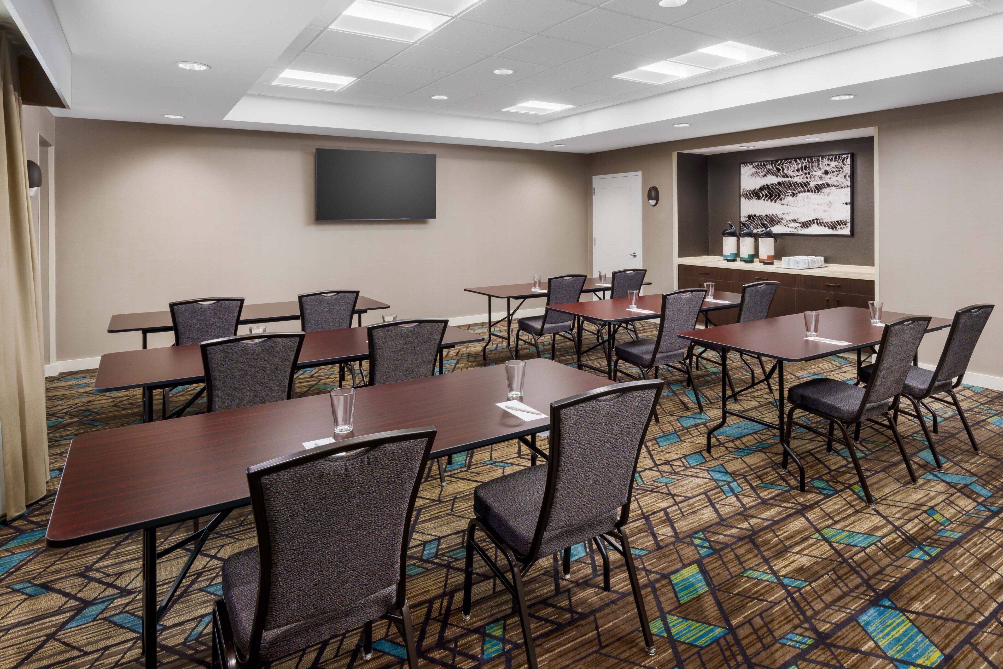 A conference room with multiple tables and chairs, a whiteboard, and a large abstract painting on the wall.